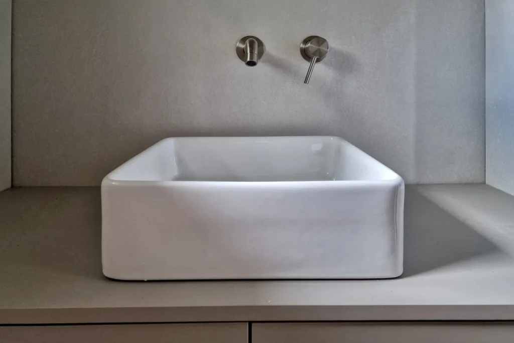 Eingelassenes weißes Waschbecken mit zwei verchromten Armaturen im Wandelement.
