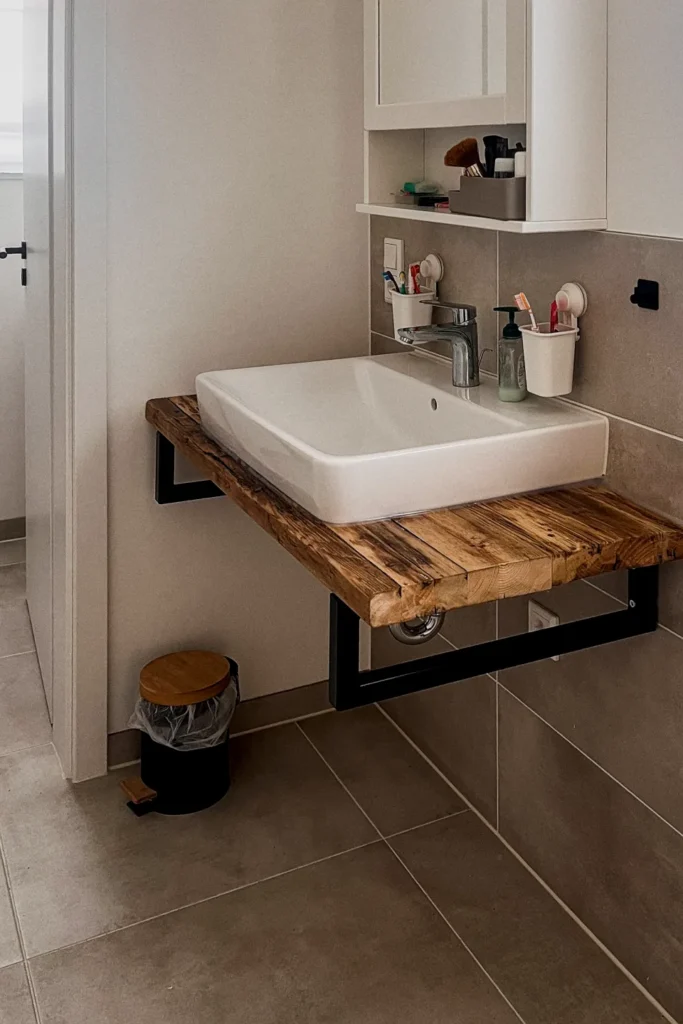 Waschbecken mit Holzplatte und Armatur in einer kleinen Gästetoilette, mit Fliesenwand und Ablagekorb.