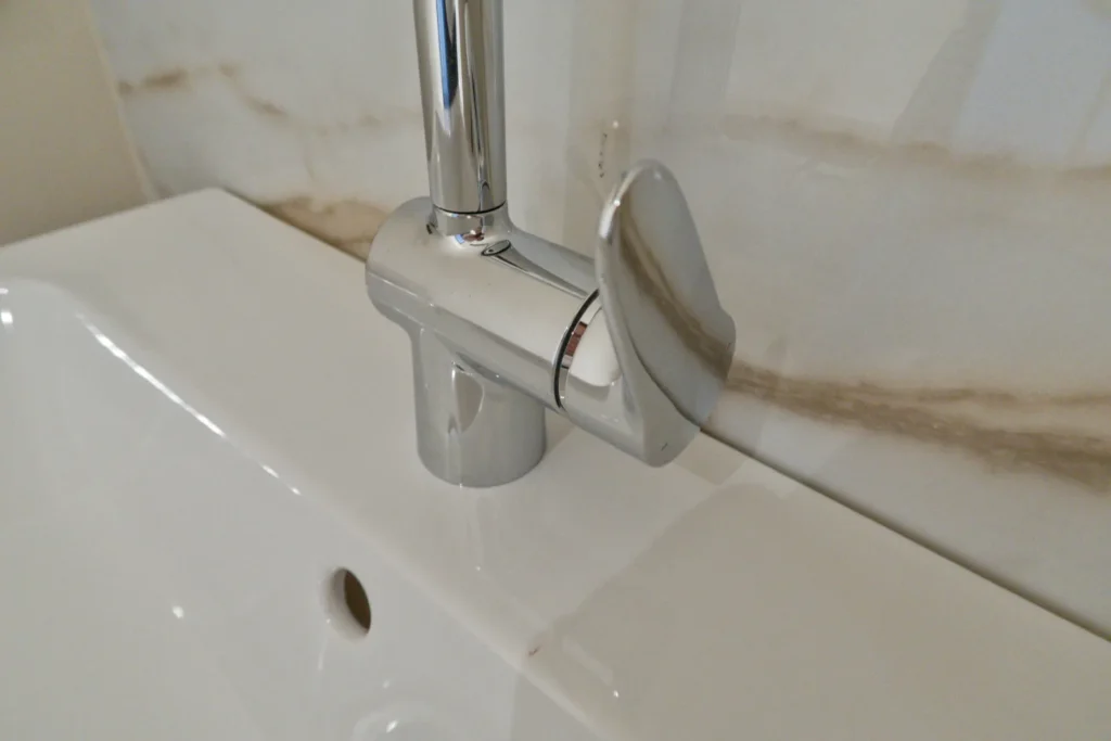 Armatur am Waschbecken mit weißer Spüle und eingebautem Ablaufventil, Detailaufnahme.