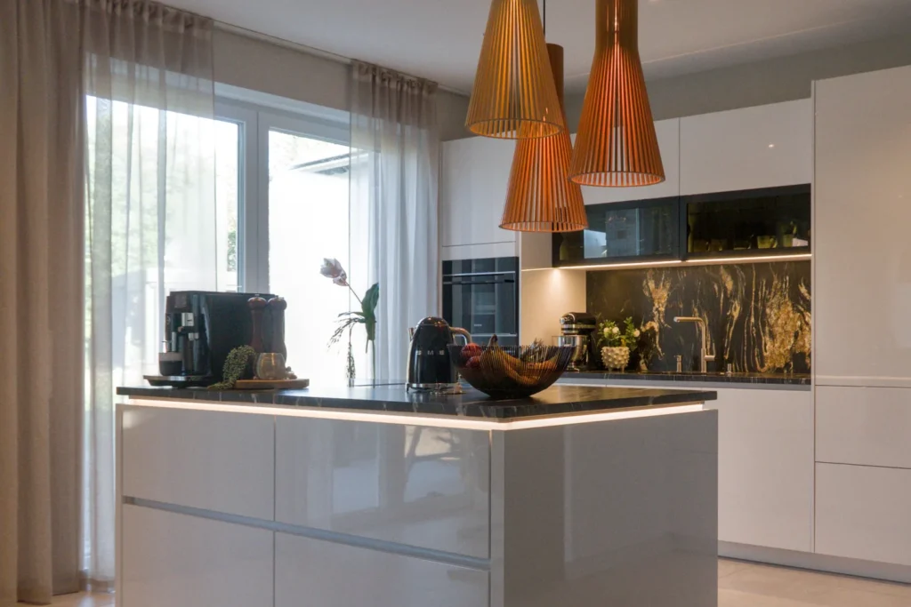 Moderne Küchenzeile mit Arbeitsplatte, Spüle, dunkler Spritzschutzrückwand und Pendelleuchten über dem Kochbereich