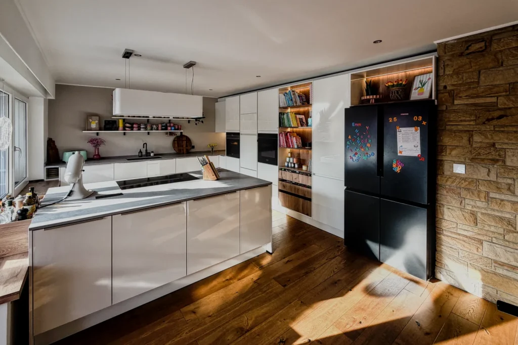 Moderne Küche mit Kochinsel, weißen Schränken, Regaleinsatz und Kühlschrank an einer Steinwand