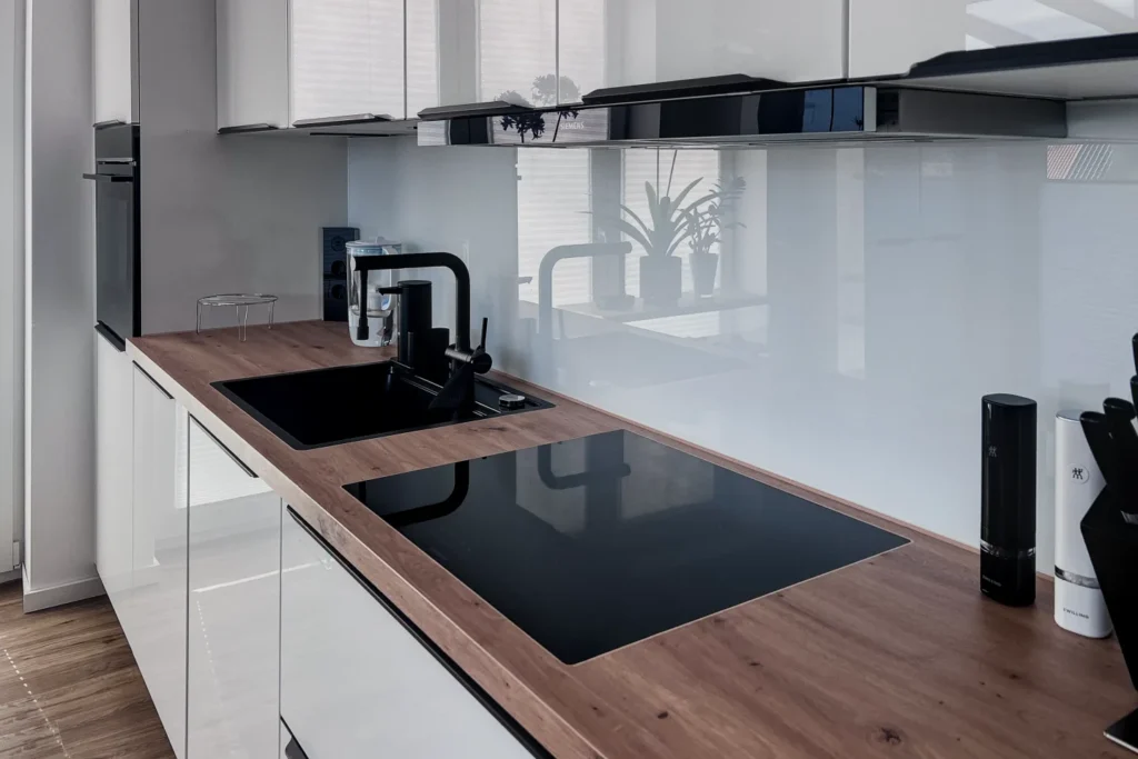 Moderne Küchenzeile mit Eckarbeitsplatte, Spüle und Induktionskochfeld sowie weißen Unterschränken und Glaskeramik-Rückwand.
