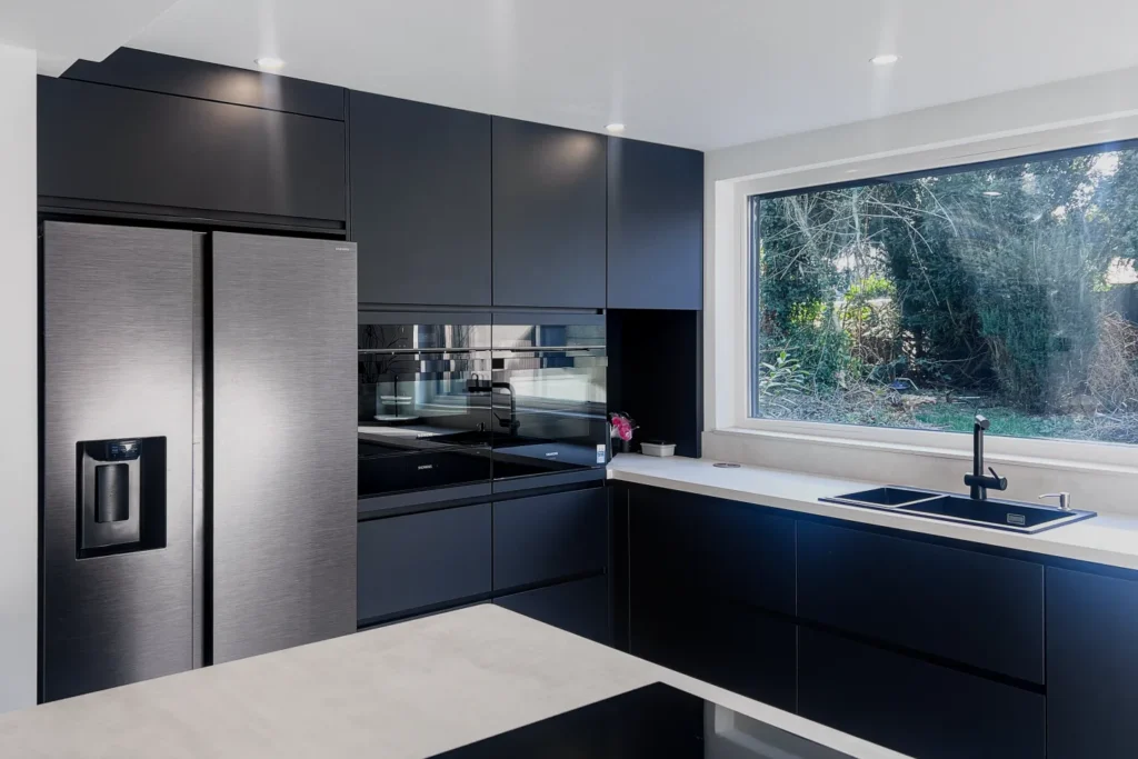 Moderne Einbauküche mit dunklen Fronten, Edelstahl-Kühlschrank, Fenster und Spülbecken an der Arbeitsplatte