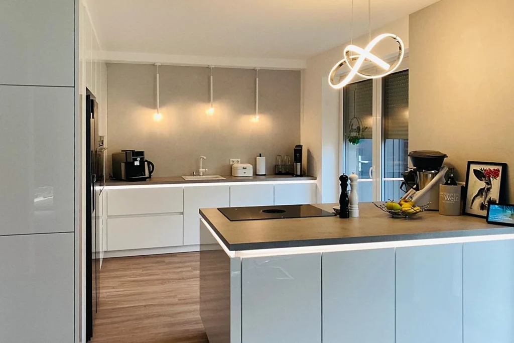 Moderne Küche mit weißen Schränken, Kücheninsel mit Spüle und hängender LED-Leuchte.