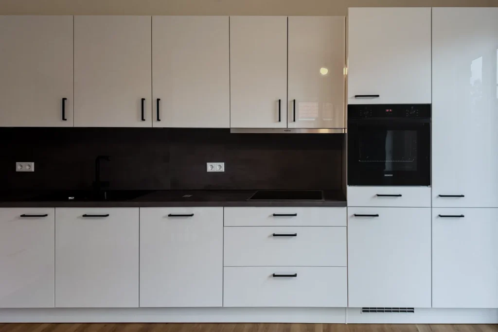 Weiße Küchenzeile mit Spülbecken, dunkler Rückwand und Backofen im Hochschrank