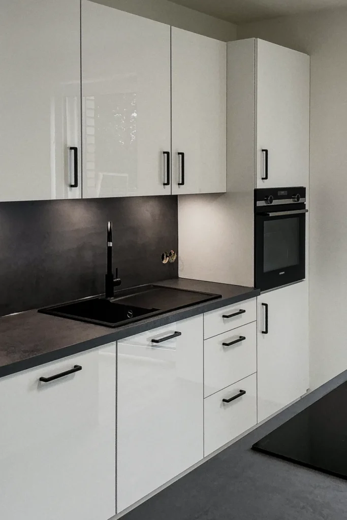 Moderne Küchenzeile mit weißen Schränken, schwarzem Kochfeld, Backofen und griffbereiten Schubladen.