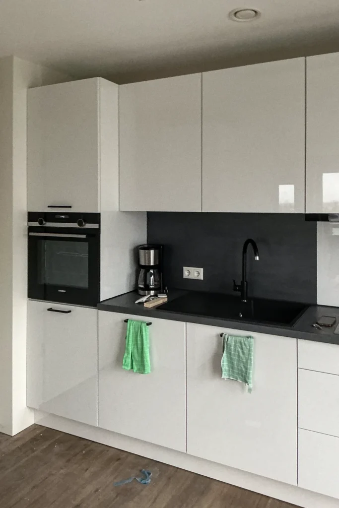Moderne Küchenzeile mit weißen Schränken, schwarzer Arbeitsplatte, Einbauherd und Spüle mit Wasserhahn.