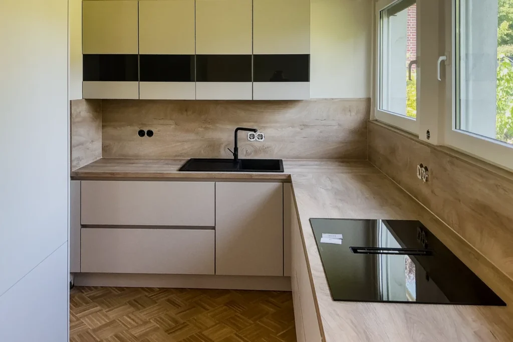 Moderne Küchenzeile mit Spüle, schwarzem Kochfeld, Oberschränken und Fenster im hellen Raum.