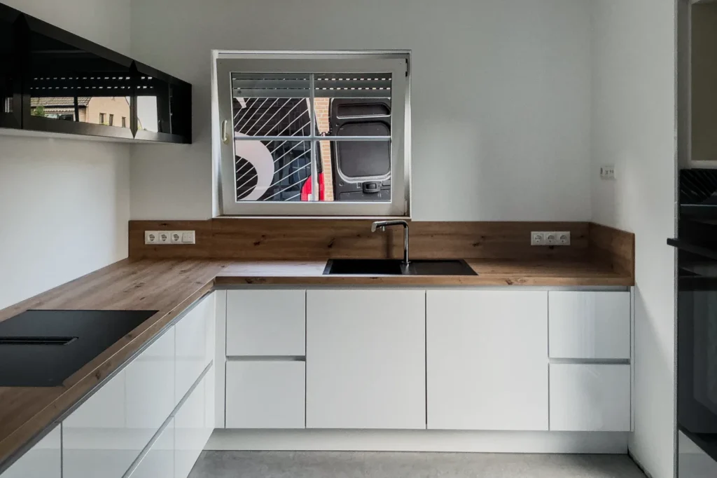 Weiße Küchenzeile mit Holz-Arbeitsplatte, Spüle und eingelassener Kochmulde mit Geschirrspüler im Unterschrank.