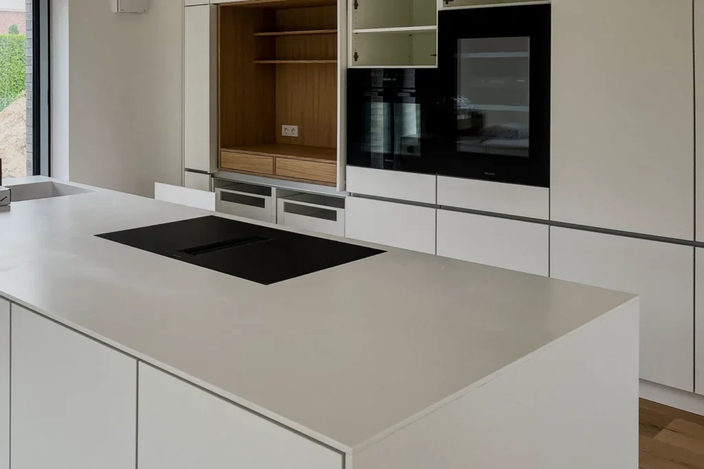 Einbauküche mit Kochfeld in der Kücheninsel, Frontschränken und integriertem Backofen im Hochschrank.