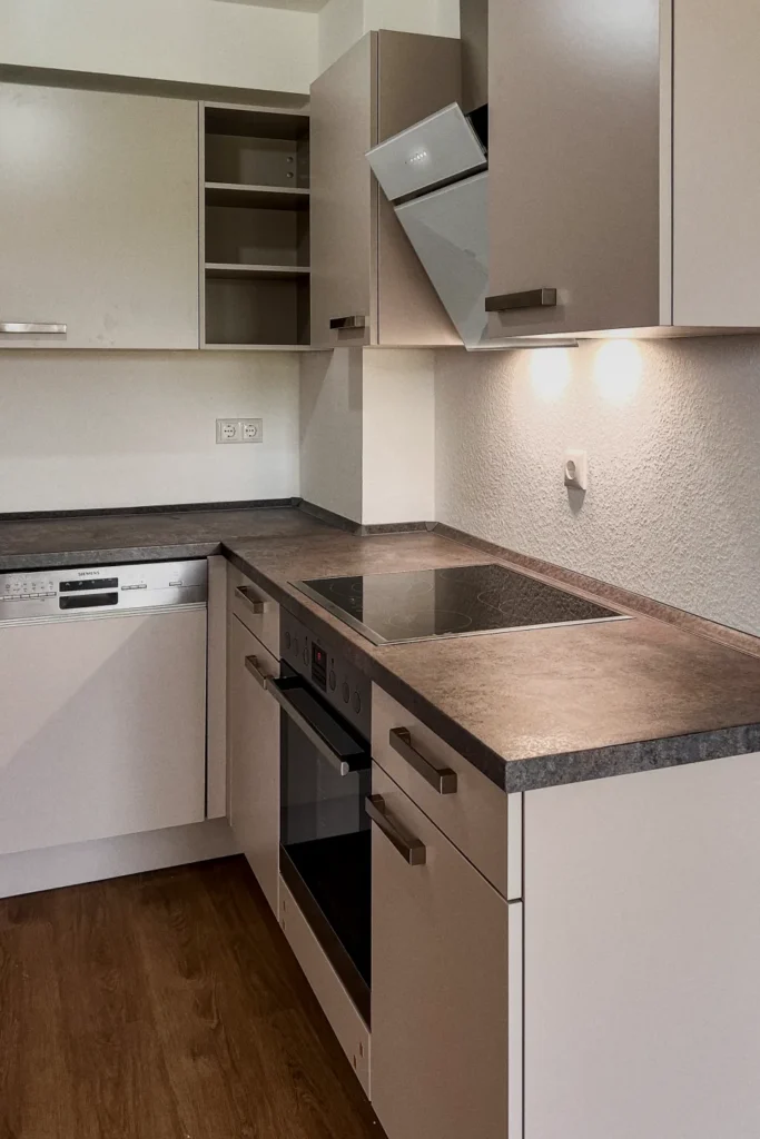 Küchenzeile mit Spüle, Herd und Dunstabzugshaube, geschlossene Unterschränke und Flachbau-Sideboard.