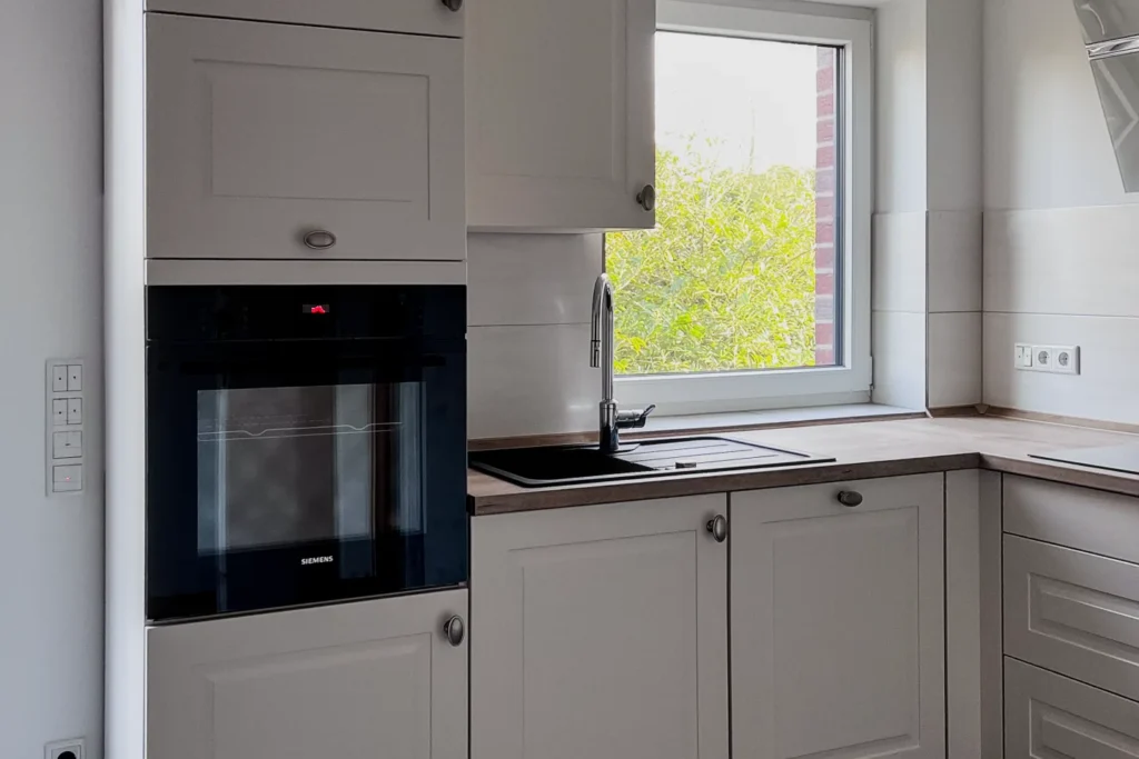Einbauküche mit Backofen, Spülbecken unter Fenster und hellen Schrankfronten