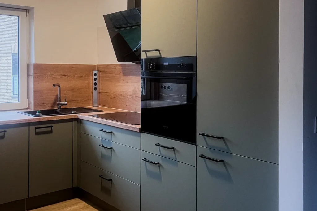 Moderne Küchenzeile mit Eckspüle, Dunstabzug und eingebautem Ofen, matte Fronten und Holzrückwand.