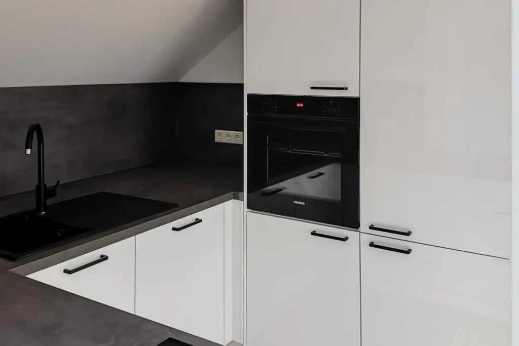 Moderne Einbauküche mit schwarzer Arbeitsplatte, Spüle und Backofen im weißen Hochschrank, Schubladen und Griffen