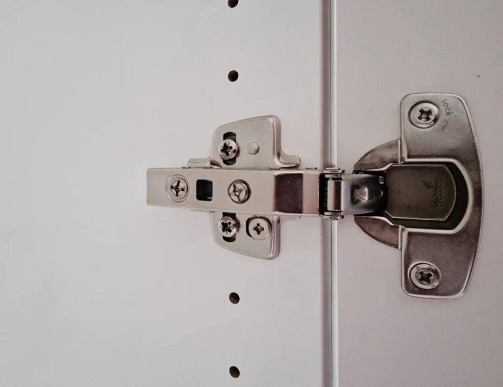 Schließmechanismus einer Schranktür mit Metall-Scharnierverschluss und Schrauben an der Türkante