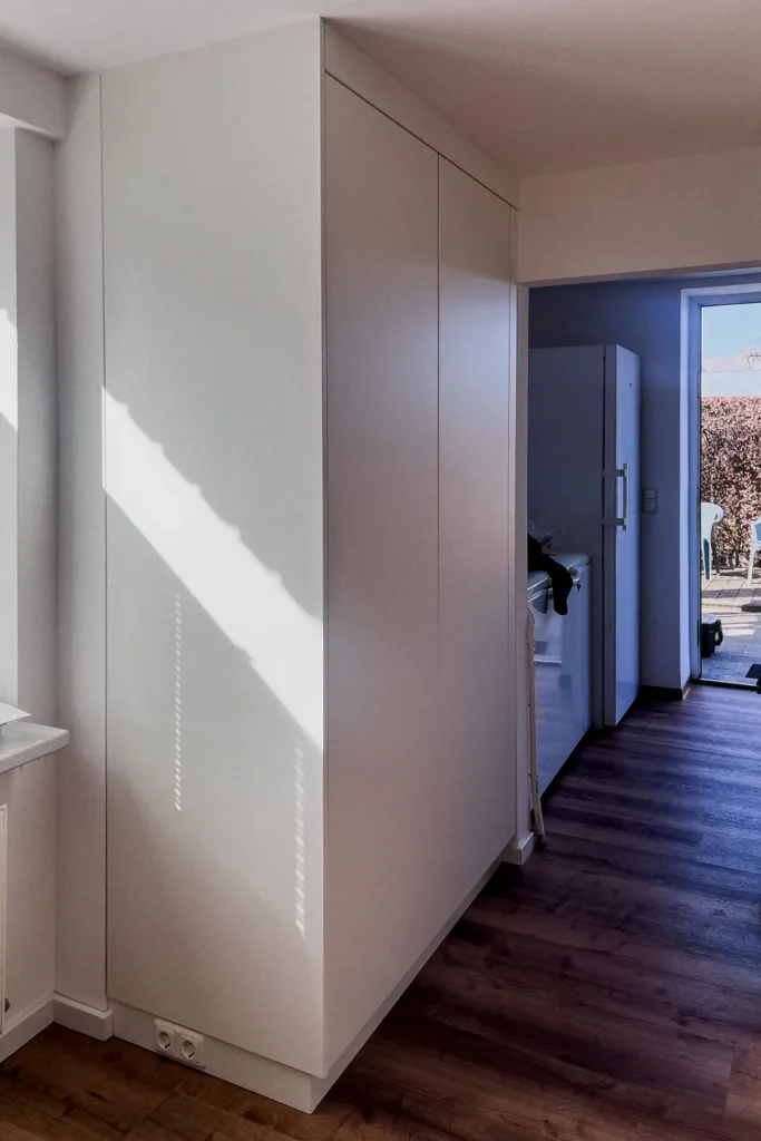 Schrank im Flur mit glatten Fronten und Griffmulden, neben einer Tür zum Wohnbereich.