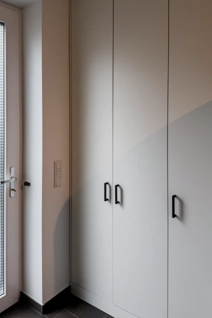 Schmaler Einbauschrank mit Griffen und vertikalen Fugen in einer Flurecke, daneben Lichtschalter und Steckdose.