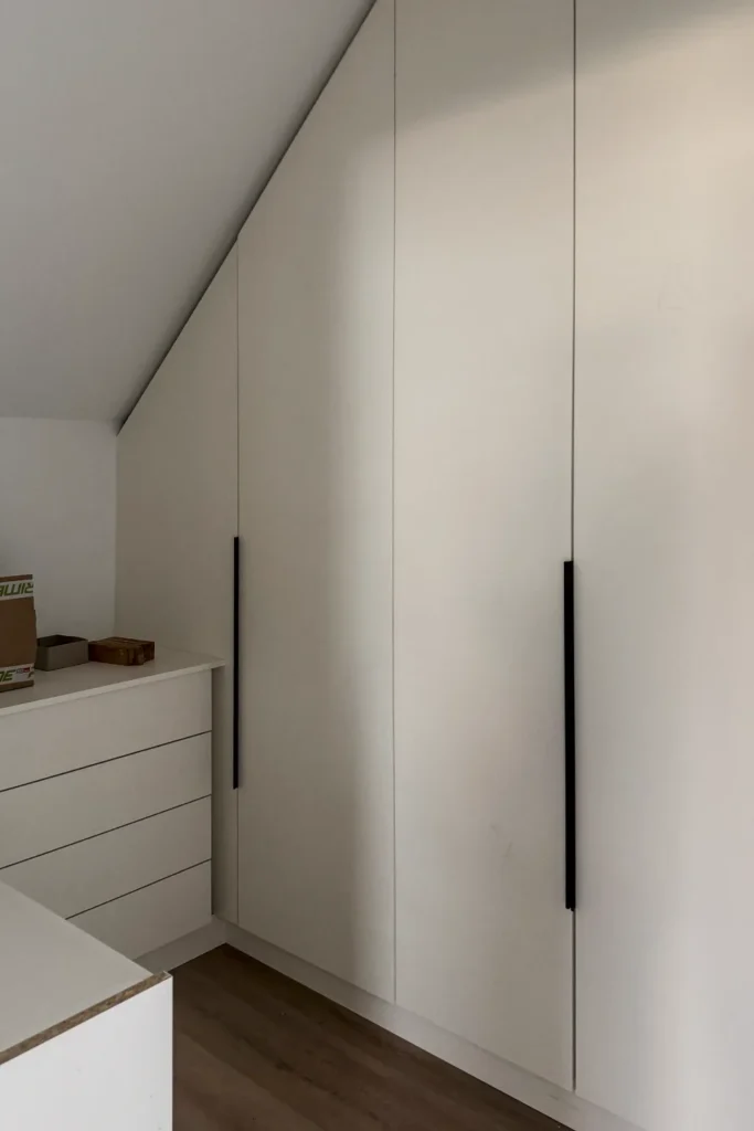 Hochschrank mit Schubladen und Küchenfronten in einer Ecke unter dem schrägen Dach, mit Griffen und Türfugen