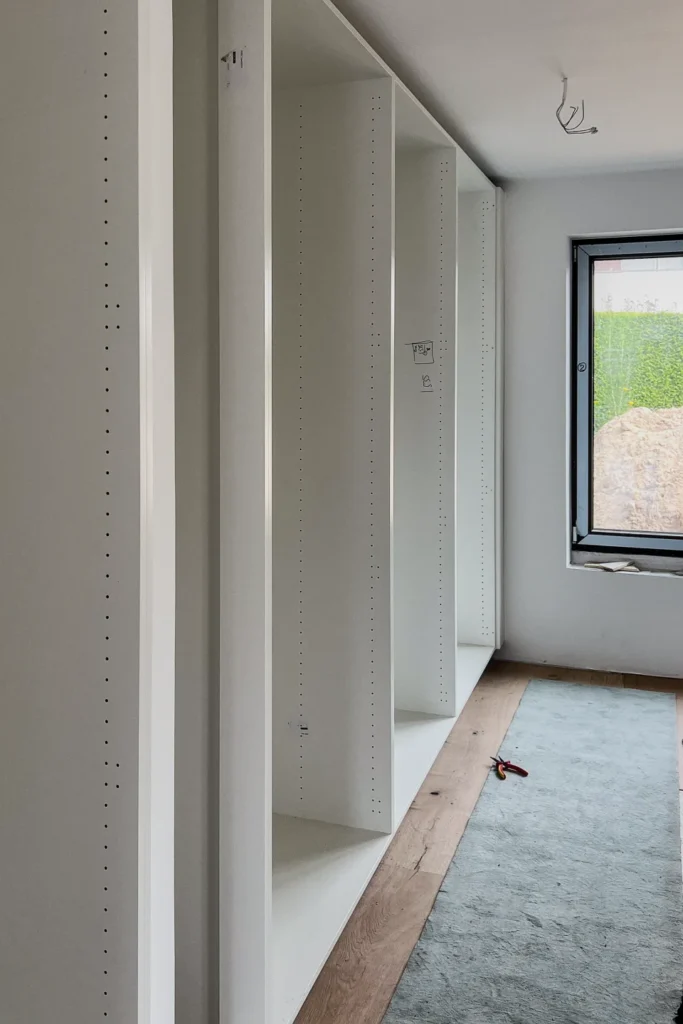 Weiße Einbauregale mit Lochraster an der Wand, Flur mit Fenster und hellem Boden während der Bauphase.