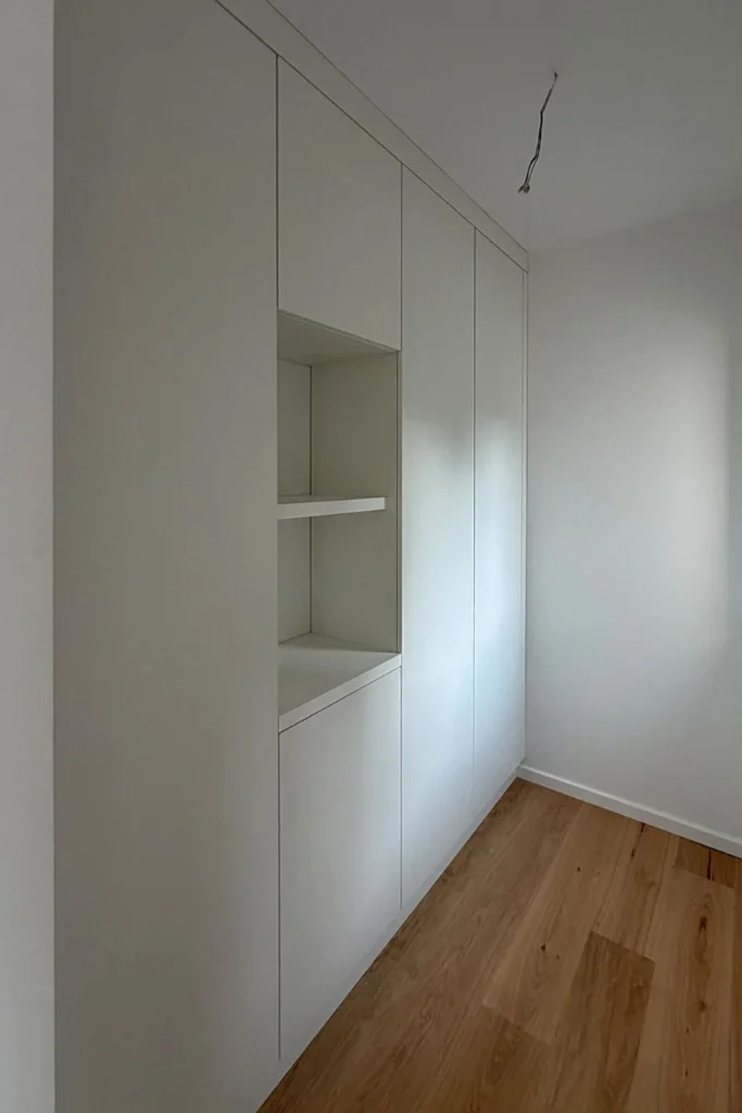 Weiße Küchenzeile mit offenen Nischen und Schublade, eingebaut in eine Wand, mit Holzfußboden.