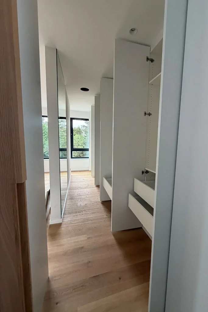 Einbauschrank im Flur mit offenen Türen und Schubladenfronten sowie Blick zum Fenster.