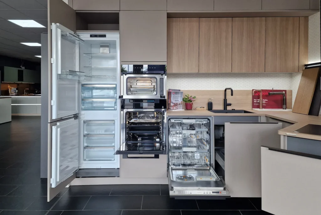 Offener Geschirrspüler und Kühlschrank in einer modernen Einbauküche mit Holzfronten und Arbeitsplatte.