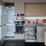 Offener Geschirrspüler und Kühlschrank in einer modernen Einbauküche mit Holzfronten und Arbeitsplatte.