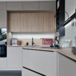 Moderne Küchenzeile mit Spüle, Armatur, Kaffeekanne und Hängeschränken, daneben integrierter Backofen.