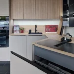 Moderne Küchenzeile mit Holz-Fronten, grauen Schränken, Spülbecken, Induktionskochfeld und Dunstabzug über der Arbeitsplatte.