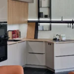 Moderne Küchenzeile mit hellen Schrankfronten, schwarzem Backofen, Spüle, Kaffeemaschine und Wandregal.