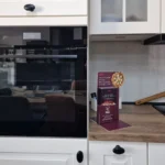 Einbaubackofen mit geöffneter Tür, daneben Küchenarbeitsplatte mit Pizzaback-Box „AEG“.