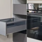 Graue Küchenschublade im geöffneten Unterschrank mit Glastür und eingebautem Küchenbereich