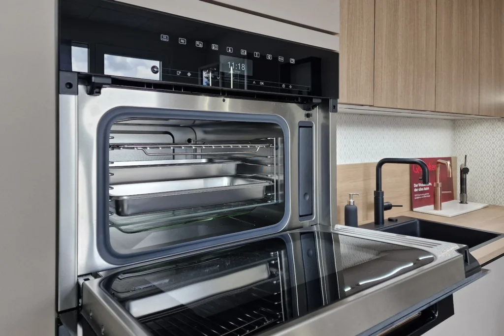Offener Einbau-Backofen mit Einschubgittern und Beleuchtung, daneben Küchenarbeitsplatte mit Spülarmatur