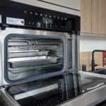 Offener Einbau-Backofen mit Einschubgittern und Beleuchtung, daneben Küchenarbeitsplatte mit Spülarmatur