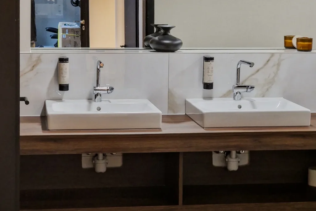 Doppelwaschtisch mit zwei rechteckigen Waschbecken, Chromarmaturen und marmorierter Wandverkleidung im Bad