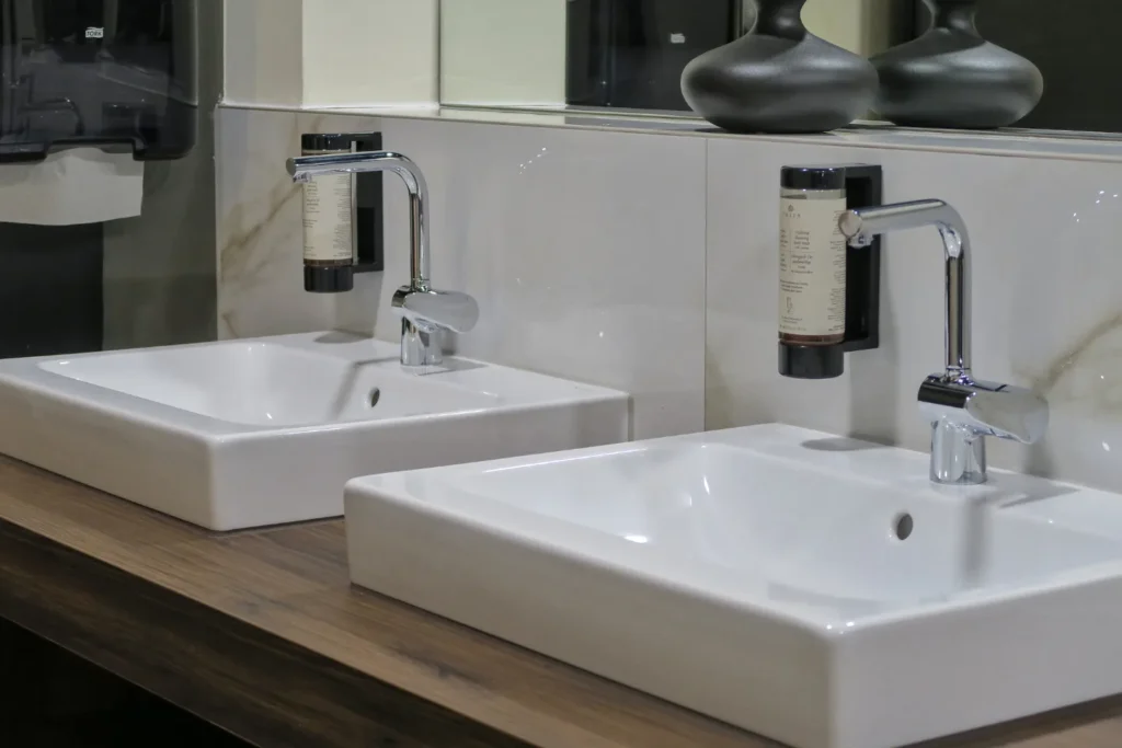 Zwei weiße Waschtische mit verchromten Armaturen und Seifenspendern in einem modernen Bad.