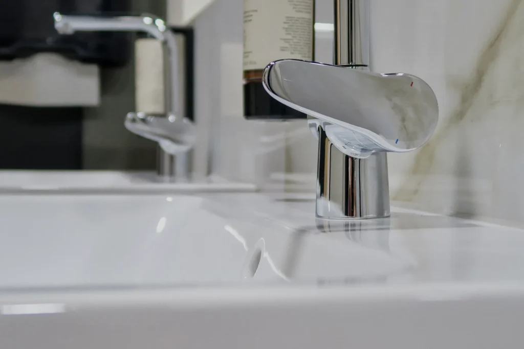 Chromierter Wasserhahn an weißem Waschbecken, Wandanschluss im Hintergrund.