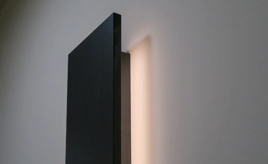 Dunkles Möbel mit senkrechtem Paneel und warmem Wandlicht im Hintergrund
