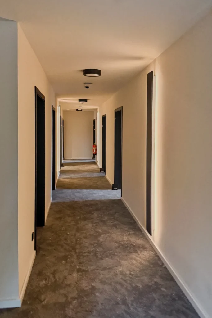 Flur in einem Hotel mit dunklen Türen, Teppichboden und eingelassenen Deckenleuchten