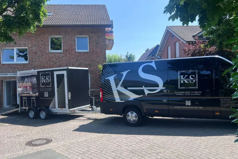 Liefer-Lkw mit großem Schriftzug „KS“ und Küchenschild im Hof vor einem Backsteinhaus